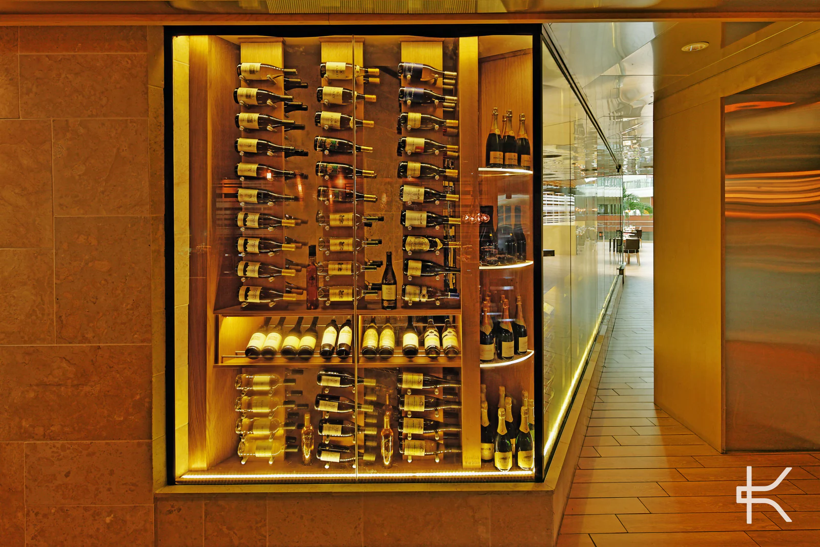 A luminous glass wine enclosure beside a receding corridor.