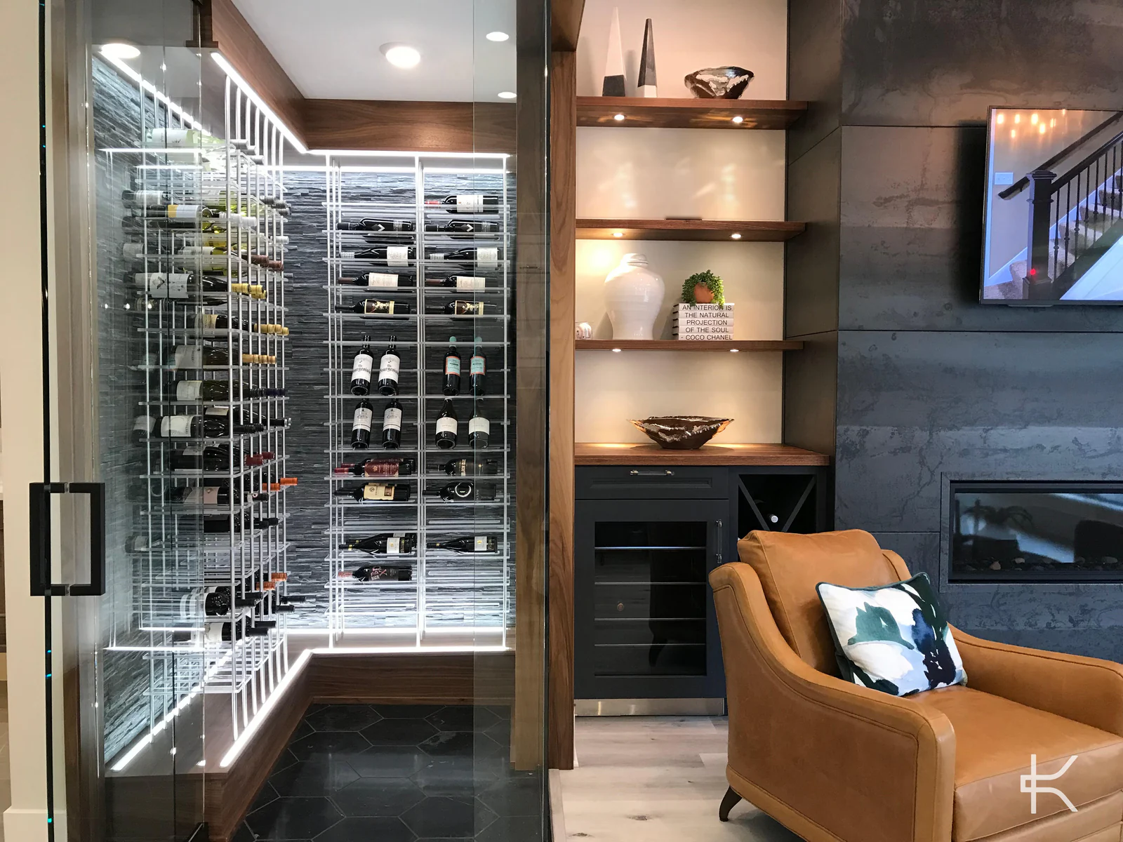 A glass-walled wine room with lit white racking beside a leather armchair.