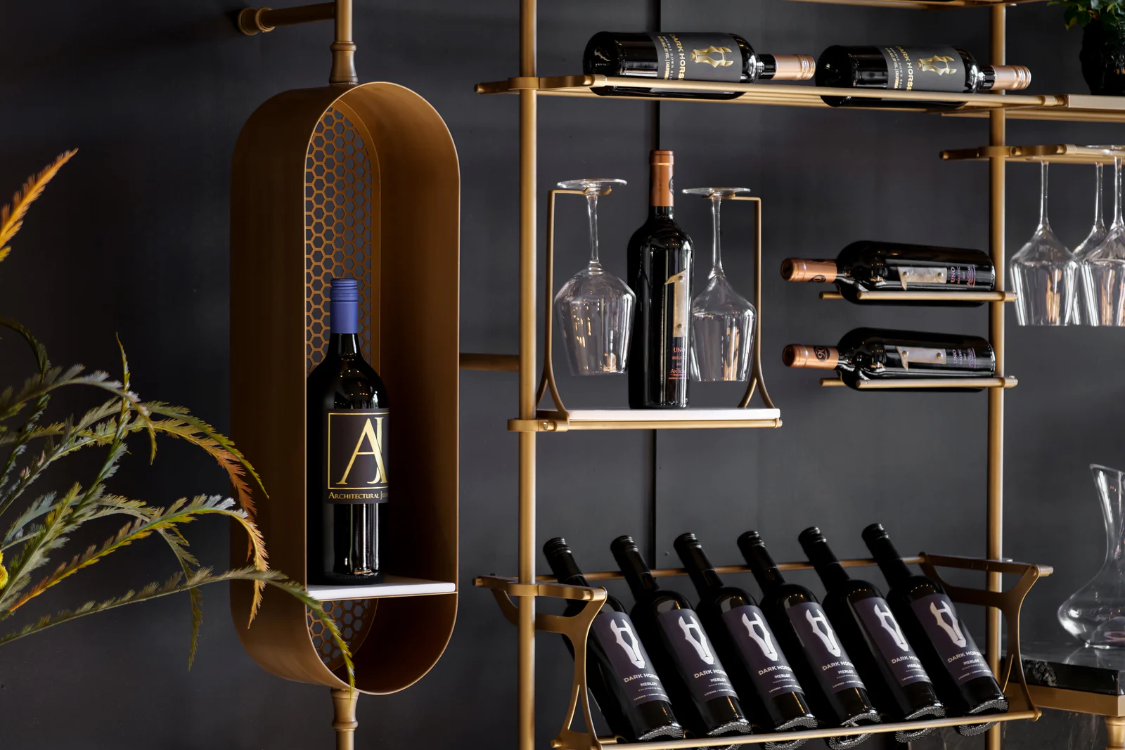 Brass-framed metal shelving holding bottles and stemware against a dark wall.