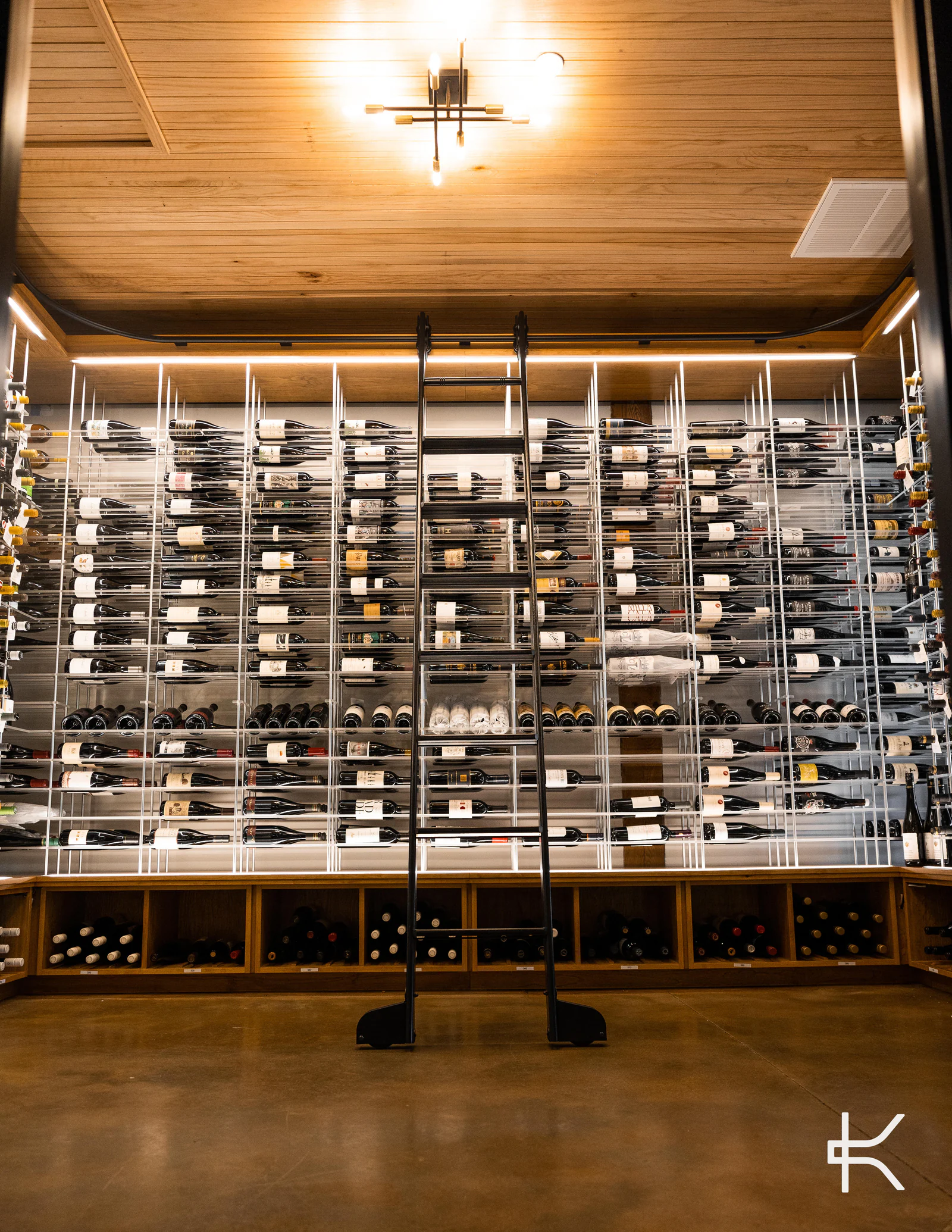 A lit wine room seen straight on, with a full-height library ladder against its racks.